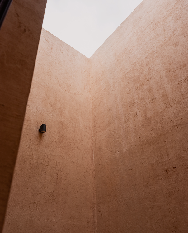 Looking up the terracotta walls of an open-sky courtyard with a single wall sconce