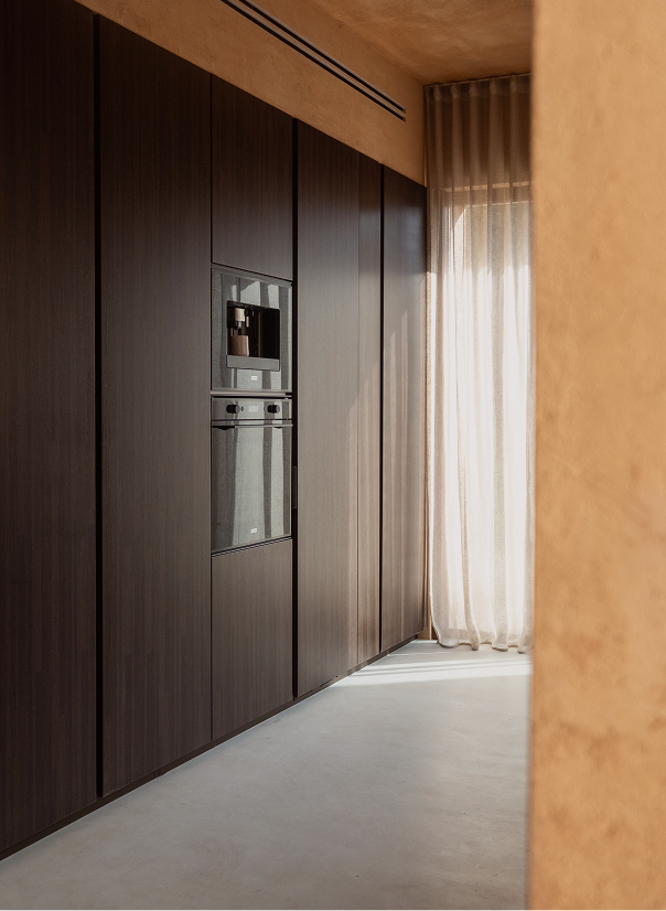 Dark wood kitchen cabinetry with a built-in oven beside a curtained window
