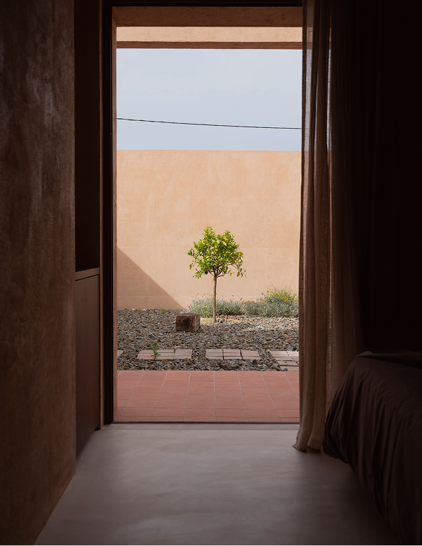 View from the bedroom through a doorway to a single tree in the terracotta courtyard