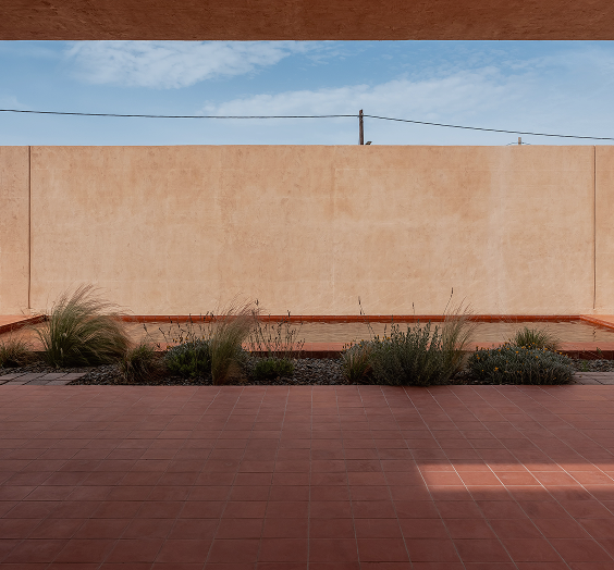 Outdoor terrace with terracotta-tile floor, planted edges and a tall earthen boundary wall
