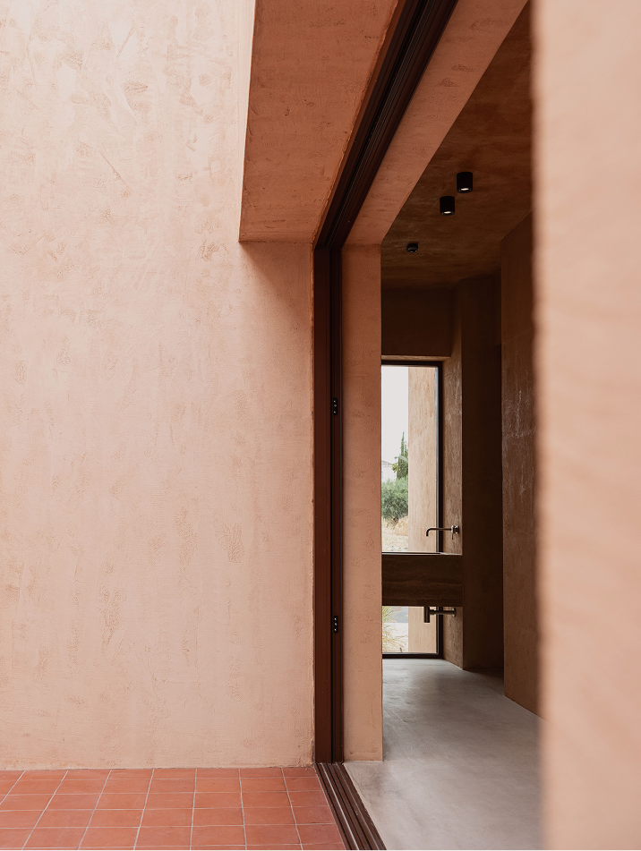 Threshold view through a tall doorway into the warm terracotta corridor beyond