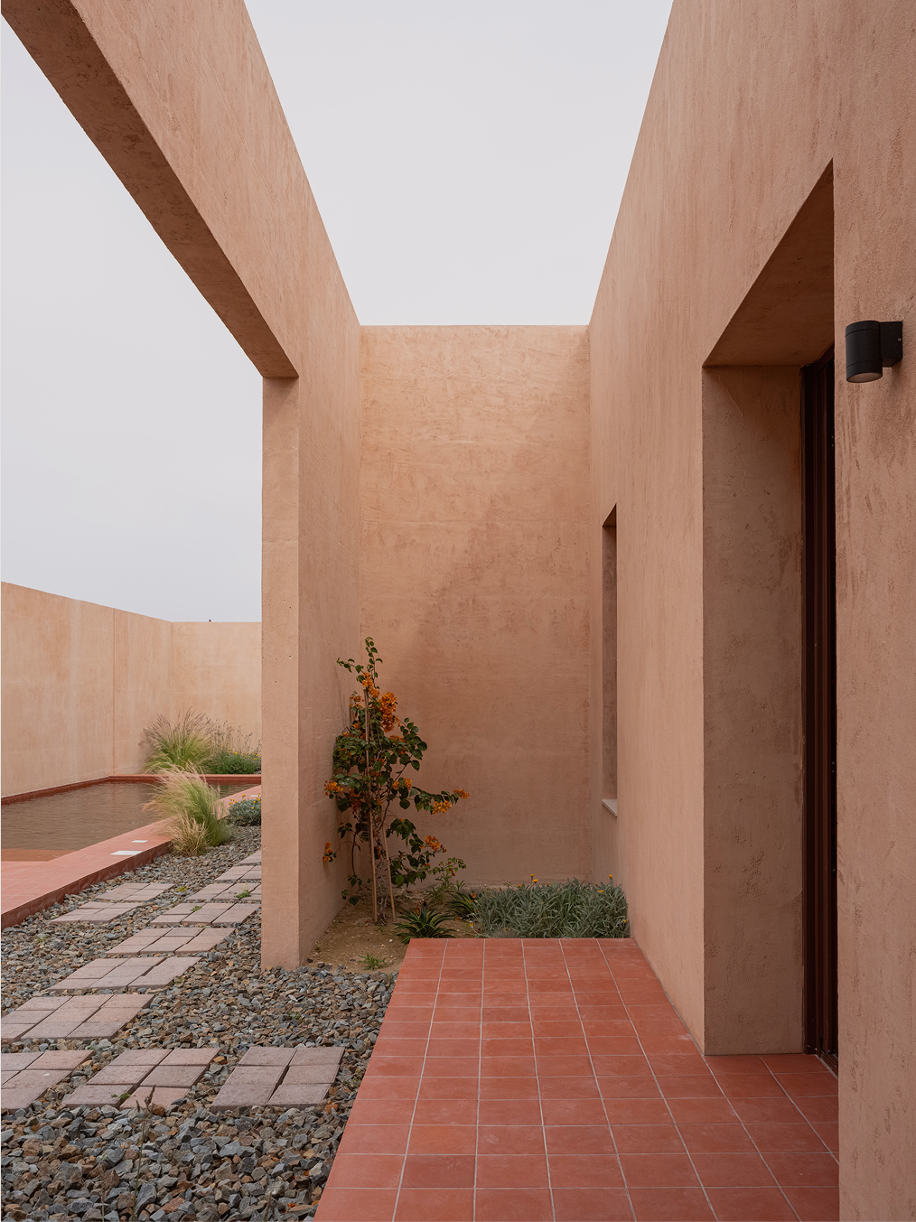 Open-air light well between terracotta volumes with a flowering shrub and gravel bed