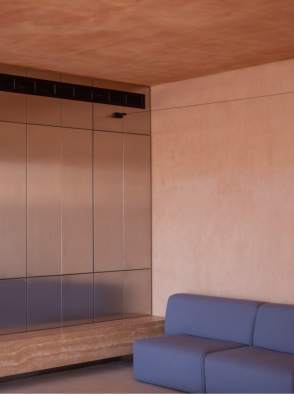 Living interior with bronze cabinetry, a built-in stone bench and a blue sofa